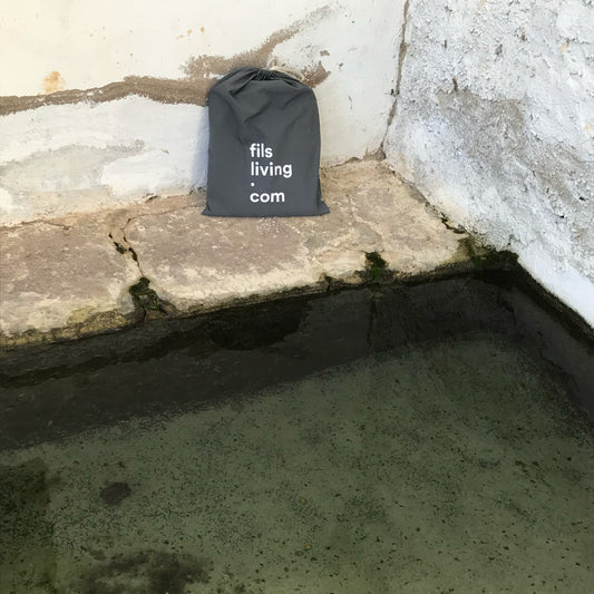 Bolsa de FILS sobre la piedra de un antiguo lavadero, evocando el lavado a la piedra de la ropa de cama